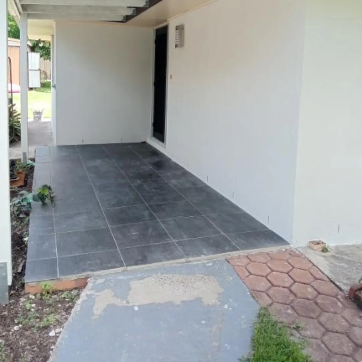 Clean rendered wall running along a tiled carport walkway