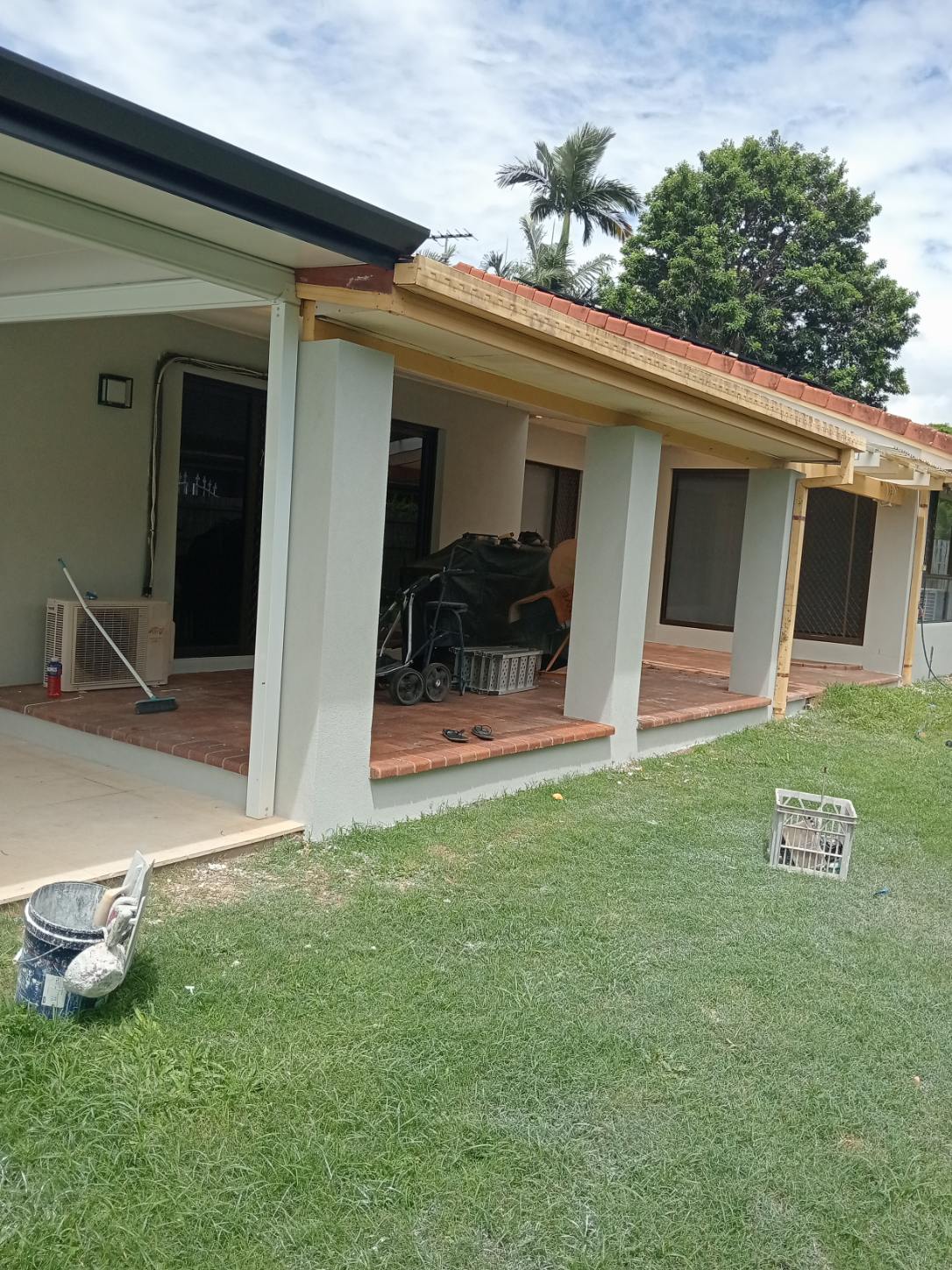 Verandah columns being rendered, with a render bucket and trowel on the lawn